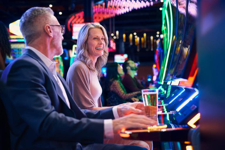 Two adults laugh while playing slot machines