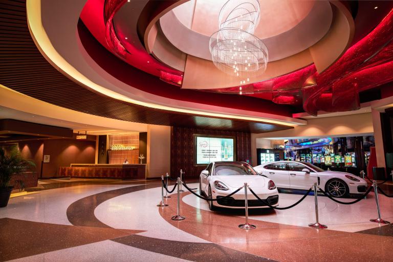 Two white sports cars sit behind velvet ropes under an abstract chandelier