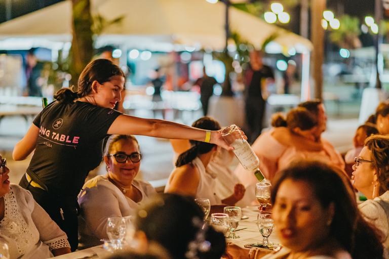 Diners converse while a server refills a glass at the Aruba Long Table Event