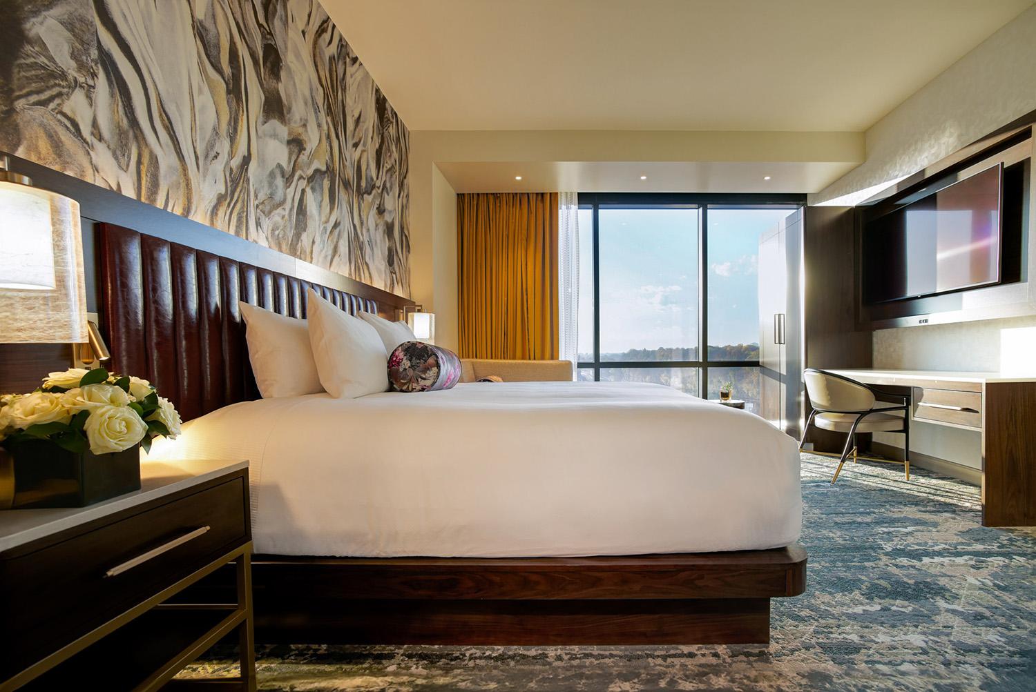 A modern hotel room with a queen bed, flat screen TV, and large window
