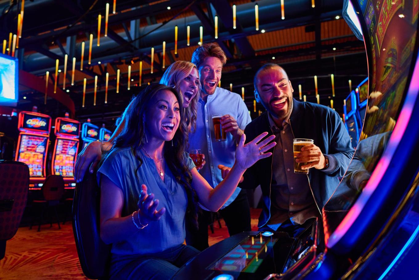 Three people excitedly gather around and watch as a woman seated at a slot machine wins big
