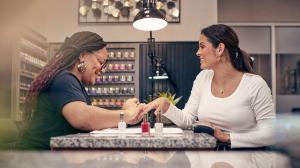 A woman gets her nails painted by a salon tech