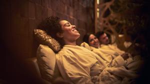 A woman wearing a white robe leans back cushioned seat and pillow