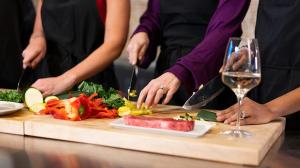 Close up view of vegetables being chopped by three sets of hands