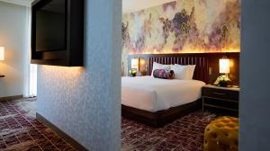 A modern hotel room with a king bed, flat screen TV and yellow ottoman
