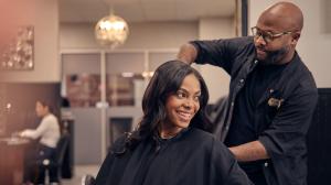 An excited young woman sits down for a haircut at a salon