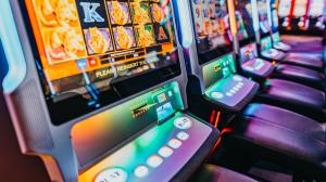 Colorful slot machines lined up in a casino, displaying vibrant screens with various symbols, next to empty chairs.