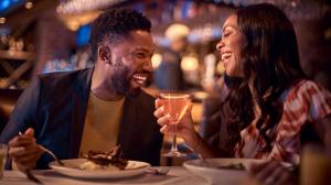 A man and a woman laughing while enjoying cocktails and a meal