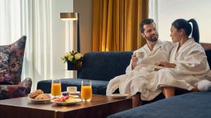 A couple wearing bathrobes enjoys breakfast in their hotel room
